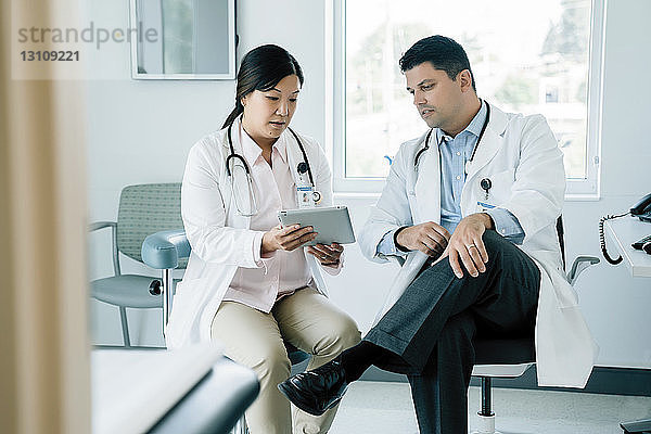 Ärzte diskutieren über Tablet-Computer  während sie im Untersuchungsraum sitzen