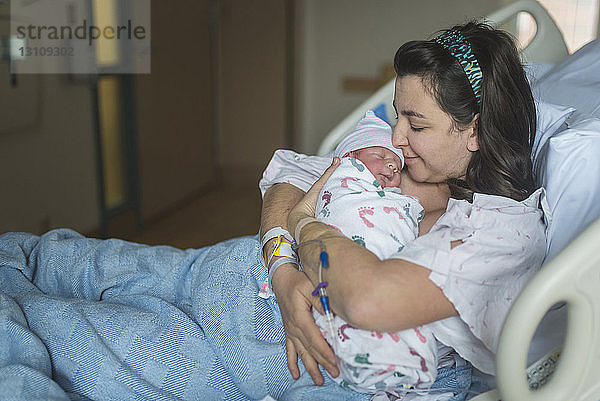 Mutter küsst neugeborenen Sohn während sie sich im Krankenhaus im Bett entspannt