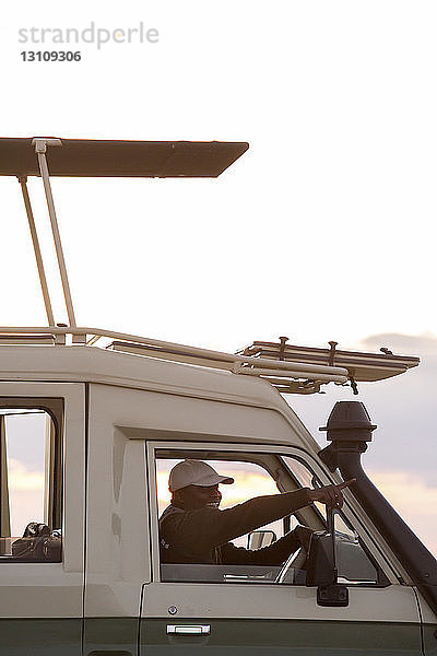 Seitenansicht eines Mannes  der beim Fahren eines Fahrzeugs im Serengeti-Nationalpark gegen den Himmel zeigt