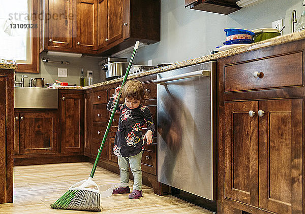 Mädchen putzt zu Hause die Küche mit einem Mopp