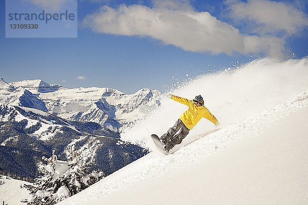 Mann beim Snowboarden auf schneebedecktem Berg gegen den Himmel