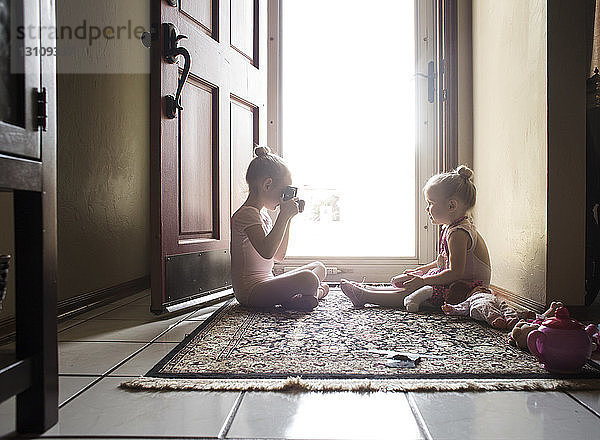 Mädchen fotografiert Schwester in Ballettkostüm  während sie an der Tür sitzt