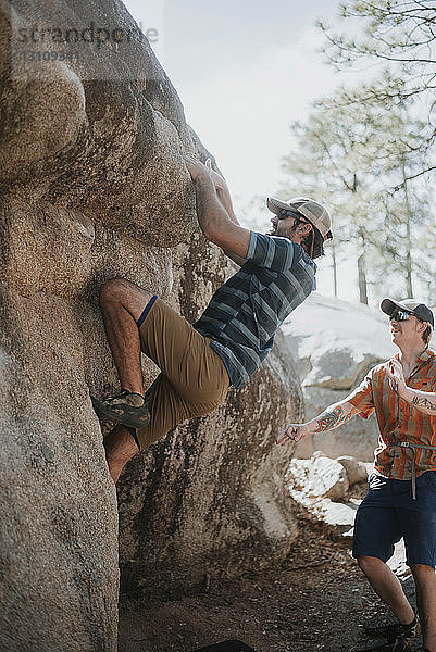 Mann hilft Freund beim Klettern am Fels gegen den Himmel im Wald