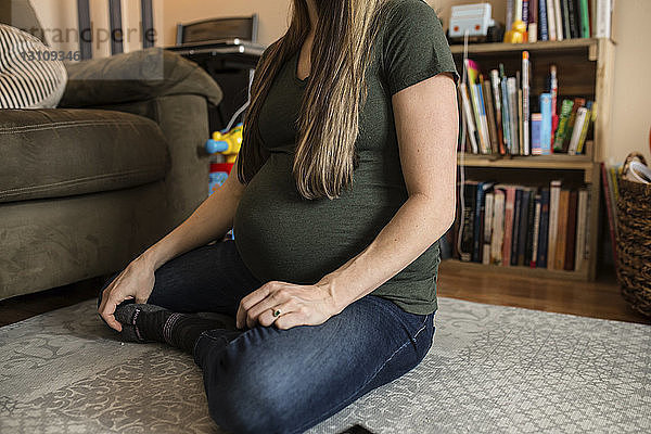 Unterer Teil einer schwangeren Frau  die zu Hause auf einem Teppich sitzt