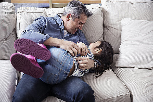 Fröhlicher Vater und Tochter genießen zu Hause auf dem Sofa