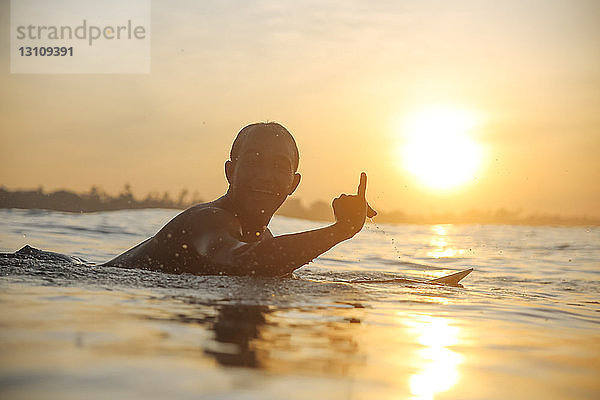 Porträt eines Mannes mit Silhouette  der bei Sonnenuntergang auf dem Meer gegen den Himmel surft