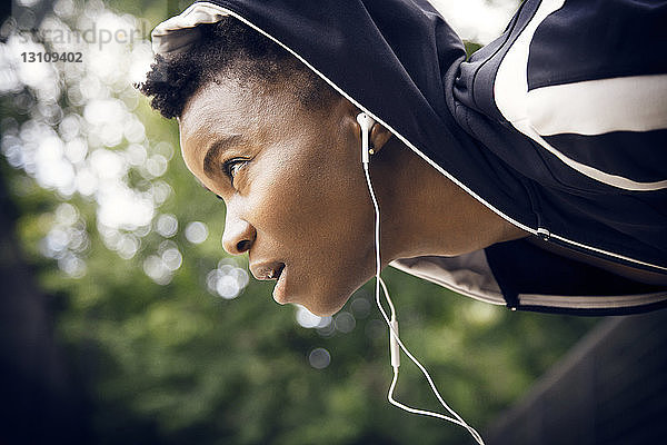 Sportlerin hört Musik über Kopfhörer  während sie im Park Sport treibt
