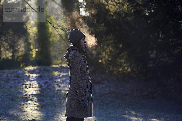 Seitenansicht einer Frau  die Atemdampf ausatmet  während sie im Winter im Park steht
