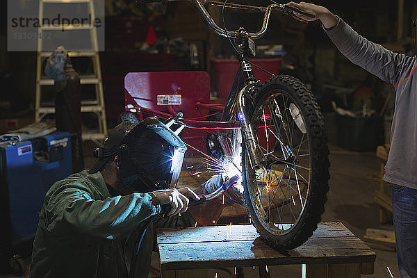 Vater und Sohn schweißen Dreirad während der Arbeit in der Werkstatt