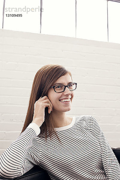 Lächelnde Geschäftsfrau sitzt im Büro an der Wand
