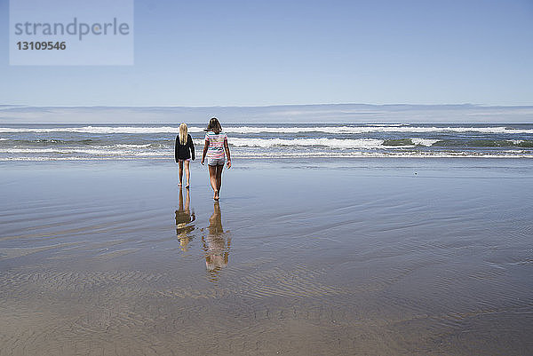 Rückansicht von Mädchen  die am Strand am Ufer gegen den Himmel laufen