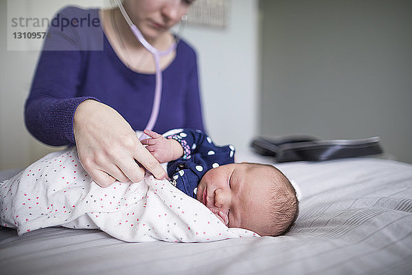 Hebamme untersucht neugeborenes schlafendes Mädchen mit Stethoskop am Bett zu Hause