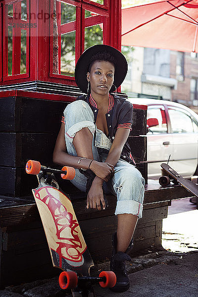 Porträt einer jungen Frau  die an Skateboards auf einer Stützmauer sitzt