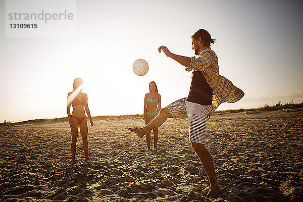 Freunde spielen Fussball am Strand gegen den Himmel