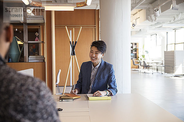 Lächelnde Geschäftsfrau diskutiert mit männlichem Kollegen im Büro