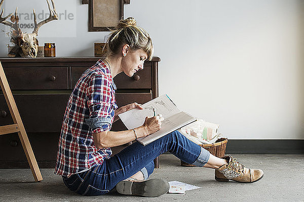 Konzentrierte Künstlerin  die zu Hause sitzend im Buch zeichnet