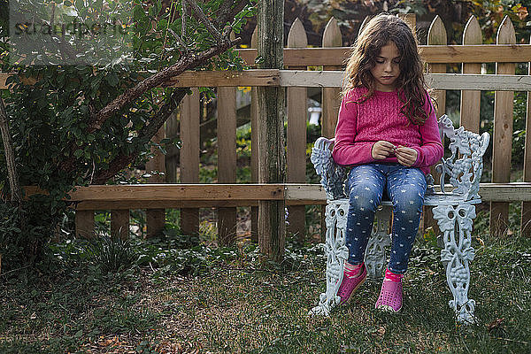 Trauriges Mädchen sitzt auf einem Stuhl im Hof