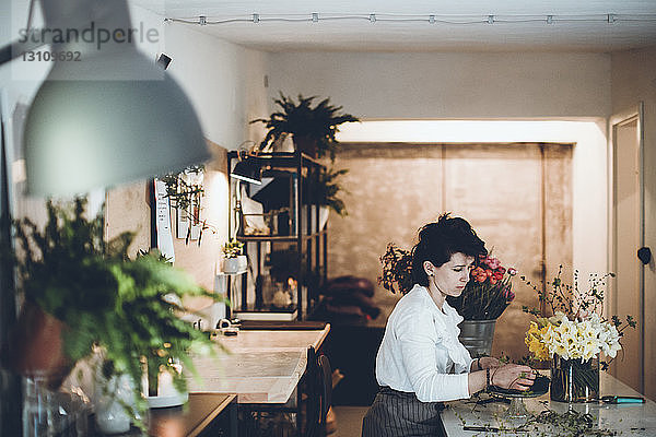 Seitenansicht eines Floristen  der Pflanzenstängel auf Blumenschäumen bei Tisch im Blumenladen arrangiert