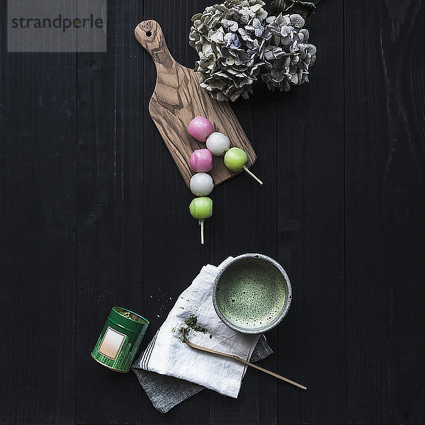 Draufsicht auf Matcha-Tee mit Süßspeisen und Hortensien auf schwarzem Tisch