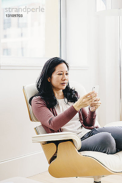 Geschäftsfrau benutzt Smartphone  während sie im Büro sitzt