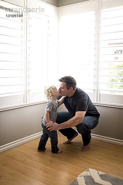 Vater und Sohn küssen sich zu Hause auf Mund gegen Fenster