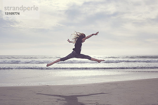 Unbeschwertes Mädchen springt am Strand gegen bewölkten Himmel
