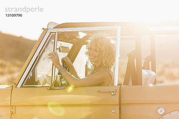 Fröhliche Frau schaut weg  während sie an einem sonnigen Tag im Geländewagen sitzt
