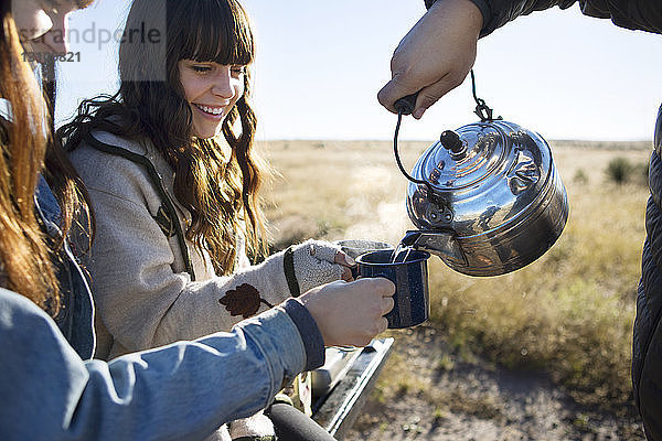 Mann gießt Wasser aus einem Teekessel in Becher  die von Freunden gehalten werden
