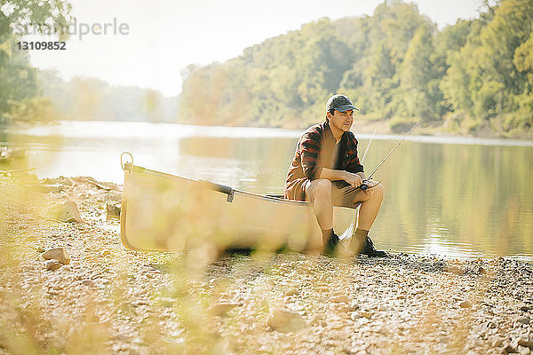 Mittelgroßer erwachsener Mann schaut weg  während er auf einem Boot am Seeufer sitzt