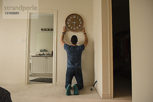 Rückansicht eines Mannes  der zu Hause eine Uhr an der Wand befestigt