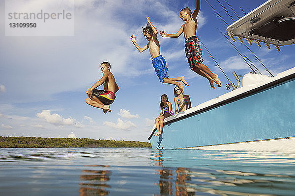 Niedrigwinkelansicht von glücklichen Jungen  die vom Boot auf See gegen den Himmel springen