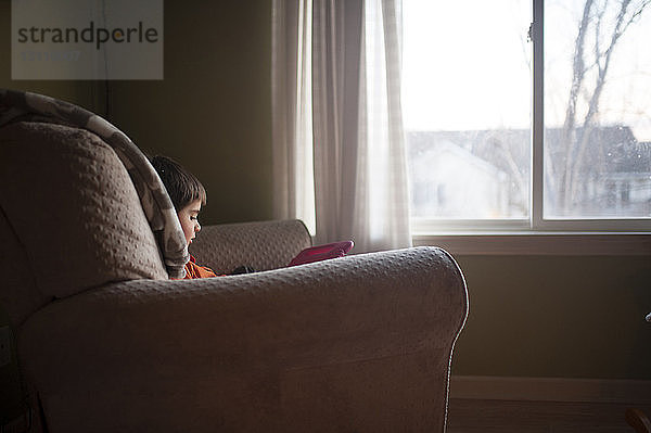 Junge spielt mit Spielzeug  während er auf einem Stuhl am Fenster sitzt