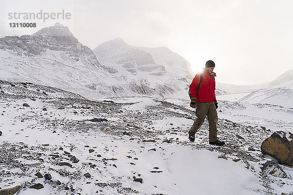Männlicher Wanderer wandert bei nebligem Wetter durch schneebedeckte Landschaft