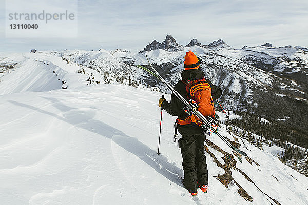Rückansicht eines auf einem schneebedeckten Berg stehenden Wanderers mit Rucksack und Ski