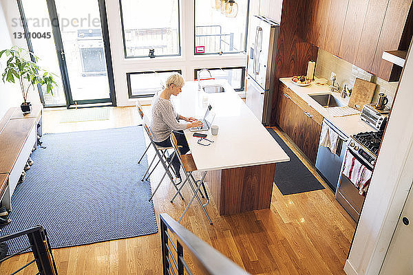 Hochwinkelansicht einer älteren Frau mit Laptop am Küchentisch zu Hause