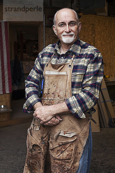 Zuversichtlicher Senior-Handwerker steht vor der Werkstatt