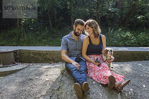 Romantisches Paar mit Welpe auf einem Felsen im Wald sitzend