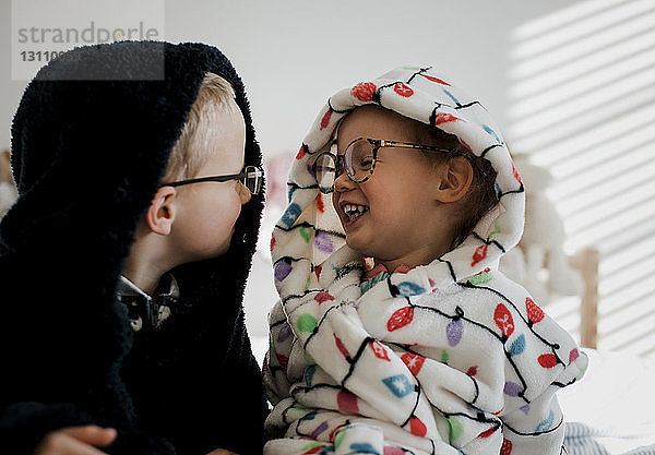 Glückliche Geschwister in warmer Kleidung  die sich gegenseitig im Schlafzimmer anschauen