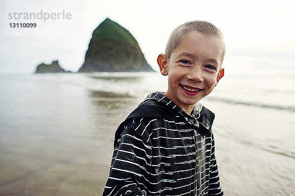 Porträt eines glücklichen Jungen  der am Strand gegen den Himmel steht