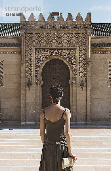 Rückansicht einer Frau  die an einem sonnigen Tag vor einem historischen Gebäude steht