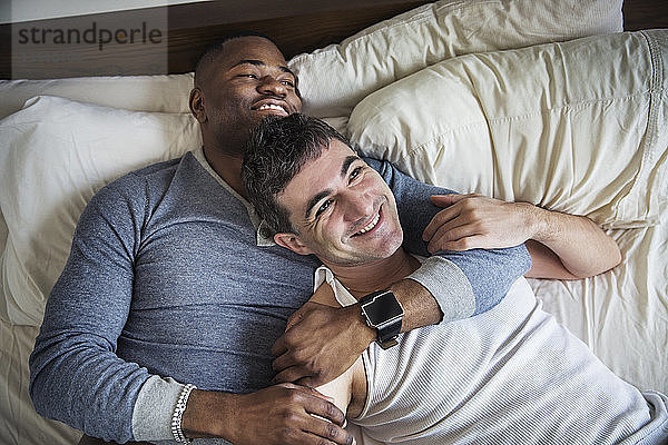 Draufsicht auf ein glücklich verliebtes schwules Paar  das auf dem Bett liegt