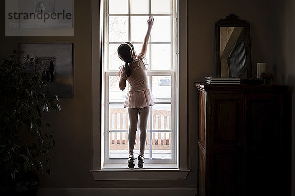 Rückansicht eines Mädchens im Ballettkostüm  das zu Hause das Fenster schließt