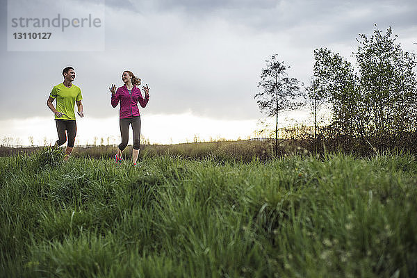 Glückliche Freunde unterhalten sich beim Joggen auf einem Grasfeld