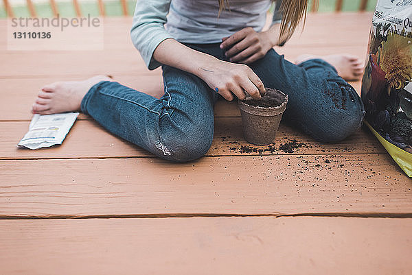 Unterer Teil eines Mädchens pflanzt Samen in einen Topf  während es auf der Veranda sitzt