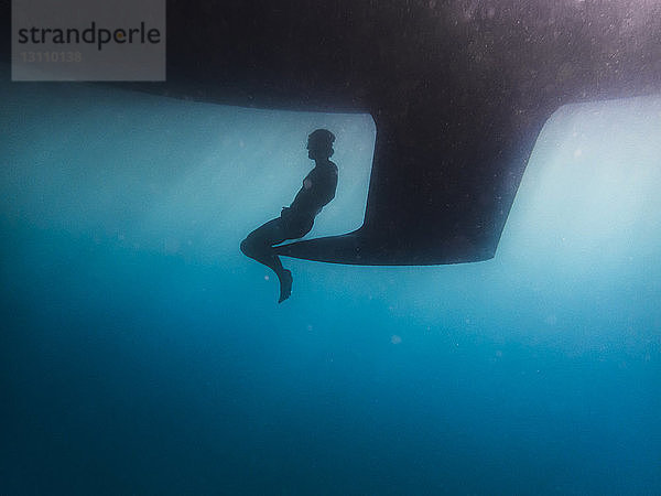 Silhouetten-Mann sitzt auf Kiel unter Wasser