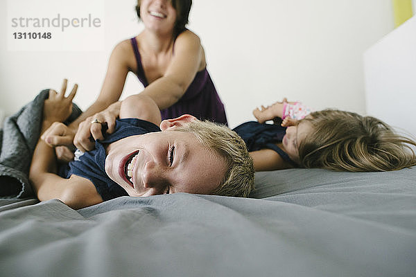 Glückliche Mutter spielt mit Kindern im Bett