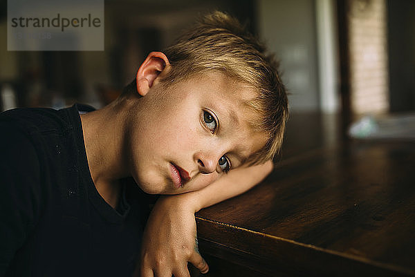 Porträt eines ernsthaften Jungen  der zu Hause mit dem Kopf auf dem Tisch liegt