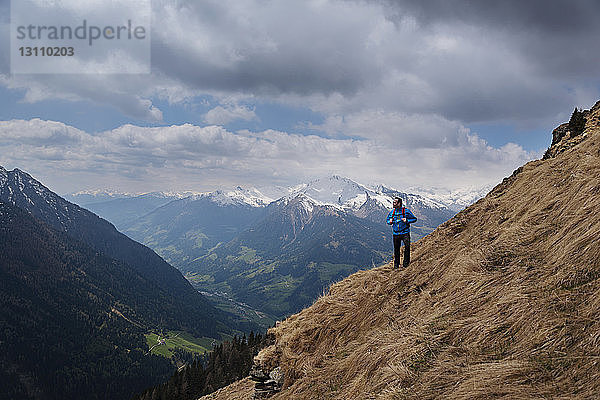 Nachdenklicher männlicher Wanderer steht auf Berg gegen wolkigen Himmel