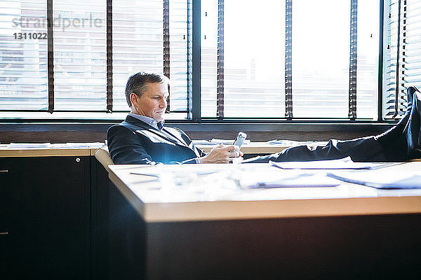 Geschäftsmann benutzt Mobiltelefon während er sich im Büro entspannt