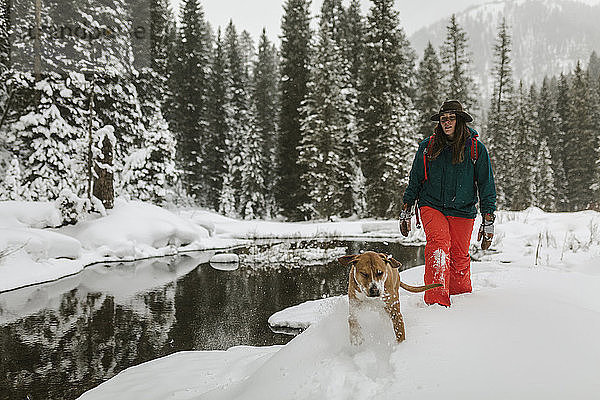 Frau mit Hund beim Spaziergang auf schneebedecktem Feld im Wald